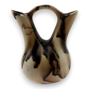 Könnte beinhalten: Eine handgefertigte Vase mit zwei Griffen und einer einzigartigen, organischen Form. Die Vase hat einen hellbraunen Grundton mit dunkelbraunen, blitzartigen Mustern. Der Griff bildet oben eine große, offene Schlaufe. Ein dekoratives Wohnaccessoire.