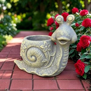 May include: A gray and yellow snail-shaped planter featuring a hollow shell with embossed flower patterns on the side. The snail has two prominent eyes on stalks and a wide, smiling mouth, crafted from a textured material with a weathered finish.