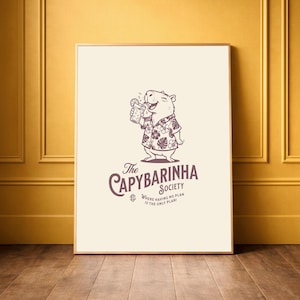 May include: Framed art print featuring a cartoon capybara wearing a Hawaiian shirt and holding a tropical drink. The print has the text "The Capybarinha Society" and "Where having no plan is the only plan!" in a brown color.