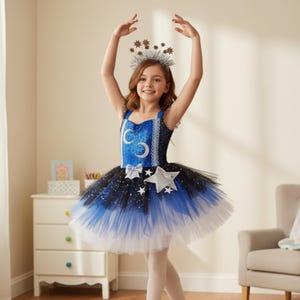 Może przedstawiać: Młoda osoba w niebiesko-czarnej sukience tutu z ozdobą w kształcie gwiazdy i srebrną koroną z gwiazd. Sukienka ma niebieski gorset ze srebrnymi akcentami i warstwową spódnicę z tiulu. Osoba ma na sobie białe rajstopy.