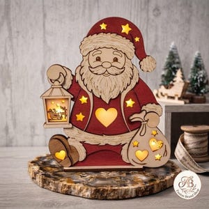 Op de afbeelding: Een houten kerstmanfiguur met een rode jas en muts, voorzien van uitgesneden ster- en hartvormen die een warm geel licht uitstralen. Het figuur houdt een lantaarn vast met een silhouet van een arrenslee en een zak met uitgesneden hartjes.