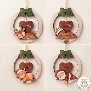 May include: Four circular wooden ornaments hanging by twine, each featuring a green bow, a dark brown heart engraved with the name Emily, and a sleeping character: a reindeer, a gingerbread person, a highland cow, and a Santa Claus figure.