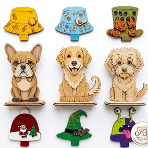 Könnte beinhalten: Eine Sammlung von neun dekorativen Holzausschnitten mit drei Hüten, drei Hunden, einer Weihnachtsmütze, einem Hexenhut und einem Monster. Die Hüte haben gelbe, blaue und grüne Designs. Die Hunde sind eine Französische Bulldogge, ein Golden Retriever.