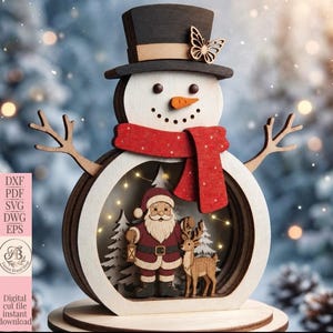 Puede incluir: Una decoración de madera en capas con forma de muñeco de nieve, que presenta un sombrero de copa negro con un detalle de mariposa, una bufanda roja y un centro hueco con una escena en miniatura de Santa y un reno entre pinos.