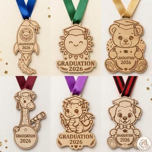 May include: Wooden graduation medals with colorful ribbons. The medals feature various designs, including a rocket, sun, bear, giraffe, dragon, and dog, all with the text "GRADUATION 2026".