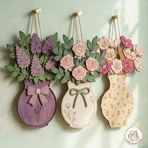 Puede incluir: Tres adornos de pared de madera con arreglos florales en jarrones. El jarrón izquierdo es morado con un lazo y lavanda, el central es crema con rosas y un lazo verde, y el derecho es de madera clara con flores rosas y patrones de corazones.