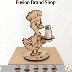 May include: Wooden duck-shaped salt and pepper shaker holder. The duck is wearing a chef's hat and uniform, holding a glass salt shaker. The base is round with floral and leaf designs. The text "Fusion Brand Shop" is at the top.