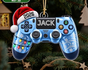 Könnte beinhalten: Ein flacher 2D-Weihnachtsanhänger aus Acryl in Form eines blauen Videospiel-Controllers. Er zeigt eine Weihnachtsmütze mit der Jahreszahl 2026, den Namen JACK sowie weihnachtliche Grafiken mit Schneeflocken, Lichterketten und Symbolen.
