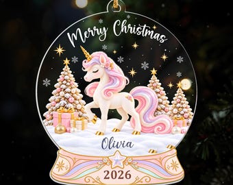 Könnte beinhalten: Ein runder, transparenter Acryl-Weihnachtsanhänger mit einem weißen Einhorn mit pastellfarbener rosa und violetter Mähne und Schweif. Das Design zeigt verschneiten Boden, drei geschmückte Weihnachtsbäume, Geschenke sowie den Text Merry Christmas, Olivia und 2026.
