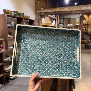 Op de afbeelding: Rechthoekig dienblad met een teal en wit schubbenpatroon. De lade heeft een lichtgekleurde rand en geïntegreerde handgrepen. De decoratieve lade is geschikt voor het serveren van eten of het uitstallen van items.