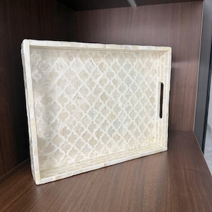 May include: Rectangular decorative tray with a white and cream mosaic pattern. The tray has a handle cut-out on one side. The tray is made of a mosaic tile pattern and is sitting on a wooden surface.