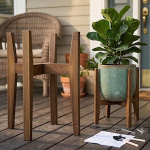 May include: A mid-century style wooden plant stand with four legs and a cross-brace design. One stand is empty, and another holds a speckled light green ceramic pot containing a green leafy plant. Assembly hardware and instructions are included.