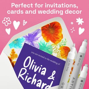 May include: A wedding invitation with floral artwork is partially visible inside a white envelope. The invitation card is purple with white text that reads "Olivia & Richard". Three silver and white ARTIS pens are in the foreground.