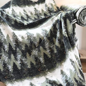 May include: A forest-themed blanket draped over a chair. The blanket features a repeating pattern of evergreen trees in shades of green and gray against a white background. The blanket is soft and cozy, perfect for snuggling up on the couch.