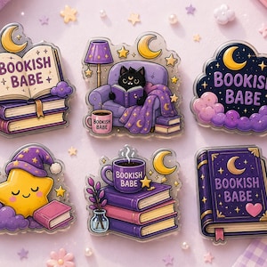 May include: Six acrylic pins featuring purple and yellow illustrations. Designs include an open book, a cat in a chair, a cloud, a sleeping star, a stack of books with a mug, and a closed book. Each piece displays the text BOOKISH BABE.