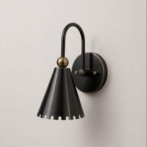 Aplique de pared moderno de latón ennegrecido con forma de cono y pantalla con borde festoneado.