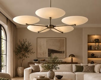 May include: A five-light chandelier featuring a central brass-toned metal stem with five extending arms, each supporting a circular, frosted white glass shade that emits a soft, warm glow, suspended from the ceiling by a matching metal rod.