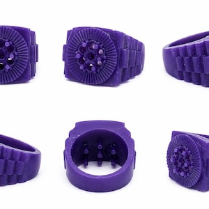 May include: A collection of six images showcasing a purple ring with a unique design. The ring features a circular centerpiece with radial lines and small circular details, and a band with a rectangular pattern. The ring is displayed from multiple angles.