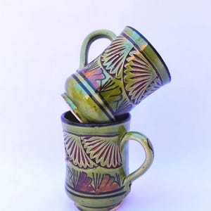 Peut inclure: Ensemble de trois mugs en céramique avec une finition mate et mouchetée. Les tasses sont de couleur crème, gris clair et gris foncé. Chaque mug a un design simple et minimaliste.