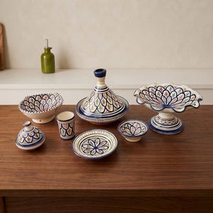 Peut inclure: Un ensemble de vaisselle en céramique comprenant un tajine, un bol sur pied à bord festonné, un petit pot avec couvercle, un gobelet, une assiette plate et deux petits bols, ornés d'un motif floral répétitif bleu, orange et marron.