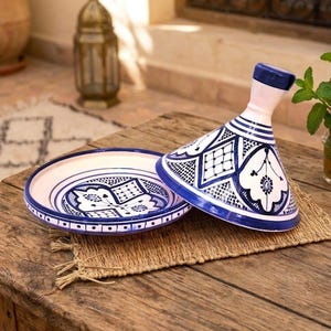 Peut inclure: Un tajine en céramique composé d'un couvercle conique et d'une base circulaire, tous deux ornés de motifs géométriques et floraux peints à la main en bleu et blanc. Le couvercle possède une poignée cylindrique haute et un bord large.
