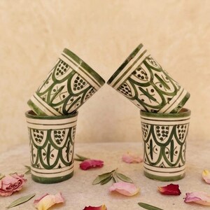 Peut inclure: Quatre tasses cylindriques en céramique ornées d'un motif peint à la main en vert, composé d'arches festonnées et de petits points sur une base crème. Deux tasses sont posées droites et deux autres sont inclinées au-dessus, formant un ensemble.