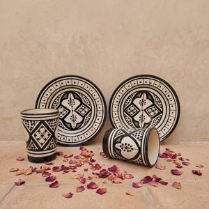 Peut inclure: Deux tasses en céramique et deux soucoupes assorties présentant un motif géométrique noir et blanc. Le design comprend des lignes, des points et des formes en losange complexes. L'ensemble est disposé avec une tasse debout et une couchée.