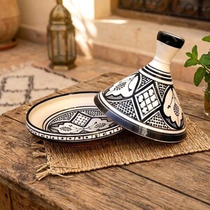 Peut inclure: Un tajine en céramique composé d'un couvercle conique et d'une base circulaire, tous deux ornés de motifs géométriques et floraux noirs et blancs complexes. Le couvercle présente un bouton noir au sommet et la base un large rebord à pois.