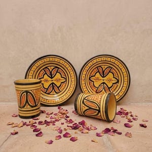 Peut inclure: Deux tasses en céramique et deux soucoupes assorties présentant une base jaune avec des motifs géométriques noirs et orange. Les tasses sont cylindriques et les soucoupes sont rondes avec un large bord. L'ensemble est orné de motifs floraux.