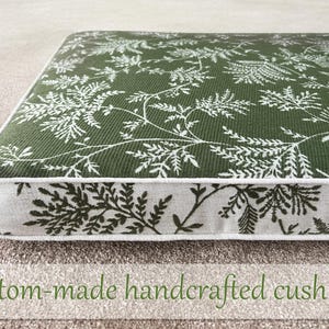 May include: A square cushion with a green background and a white fern pattern. The edges are trimmed with a white border. The text "Custom-made handcrafted cushions" is at the bottom of the image.