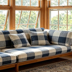 May include: A wooden framed sectional sofa with blue and white checkered cushions and pillows. The sofa is in a room with large windows and natural light. The cushions and pillows have a classic, farmhouse style.