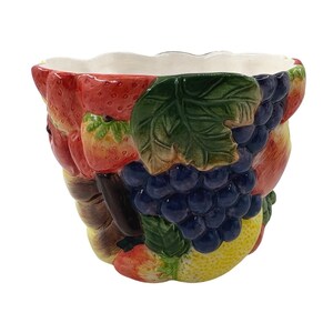 May include: A ceramic bowl featuring a three-dimensional relief design of various fruits including red strawberries, dark blue grapes, green leaves, and yellow citrus. The interior of the bowl is smooth and white with a scalloped top edge.