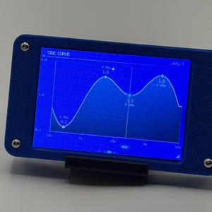 May include: A rectangular blue electronic device with a digital screen displaying a tide curve graph. The screen shows data points labeled 0.2, 1.6, 1.2, and 1.8, with the text TIDE CURVE and July 7 visible. The frame is secured by four silver screws.
