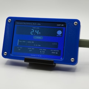 May include: A blue electronic device displaying water level data, including a reading of 2.4 ft. The screen also shows air temperature, wind speed, and air pressure. The device is connected to a green cable and mounted on a black stand.