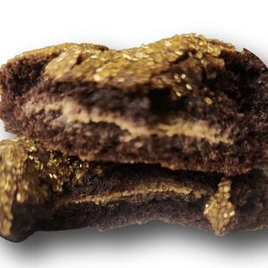 May include: Two halves of a chocolate pastry, stacked. The pastry is dark brown with a light-colored filling. The top is coated with gold-colored sprinkles. The image is set against a white background with a shadow.