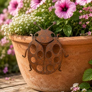 Peut inclure: Une décoration de jardin en forme de coccinelle en métal brun rouillé orne un pot de fleurs en terre cuite rempli de fleurs roses et blanches. La coccinelle a un visage souriant et de grands points ronds sur ses ailes.