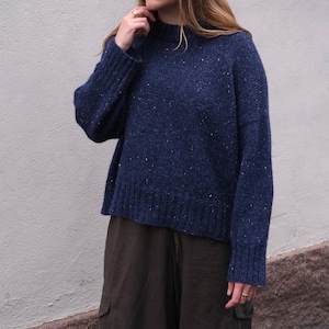 Puede incluir: Un suéter azul marino con un diseño moteado. El suéter tiene un cuello alto y mangas largas. El modelo también lleva pantalones cargo verde oliva.