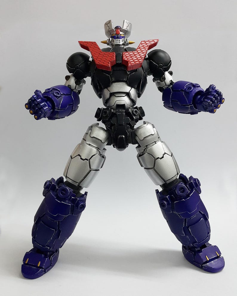 May include: A robotic action figure featuring a black, silver, and purple color scheme. The figure has a red chest plate with a honeycomb pattern, a silver head with blue and red accents, and articulated limbs with clenched fists in a standing pose.