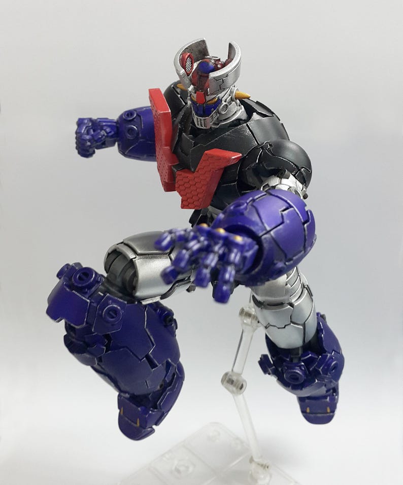 May include: A posable robot action figure featuring a black, silver, and purple color scheme with a prominent red chest plate. The figure has a metallic finish, a horned head design, and is captured in a dynamic mid-air pose with one arm extended.