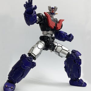 May include: A posable robot action figure featuring a dark blue and silver armored body with a prominent red chest plate. The figure has a detailed head with a silver crest, a black torso, and articulated limbs posed in a dynamic stance.