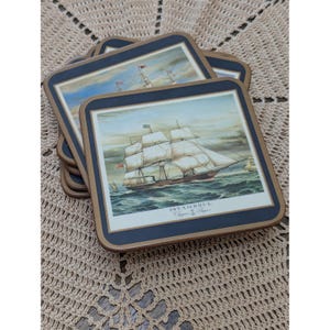 May include: A stack of square coasters with rounded corners, featuring a dark blue border and a gold-toned inner frame. The central illustration depicts a sailing ship on the ocean with the text ISTAMBOUL Clipper Ships printed below.