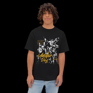 May include: A black short-sleeve t-shirt featuring a white graphic illustration of three dogs and the yellow text "Under Dog" printed on the front. The design includes small white text blocks positioned above the dog illustrations.