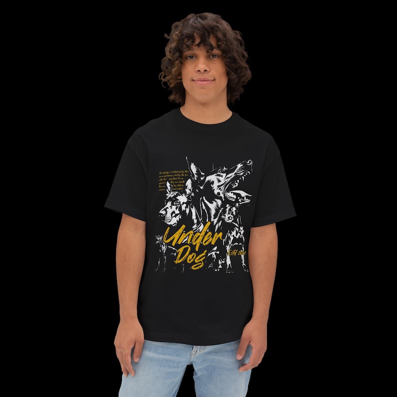 May include: A black short-sleeve t-shirt featuring a white graphic illustration of three dogs and the yellow text "Under Dog" printed on the front. The design includes small white text blocks positioned above the dog illustrations.