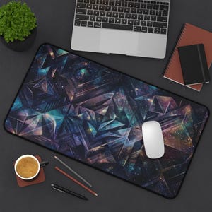 May include: A rectangular desk mat with a geometric space design in shades of blue, purple, and teal. The mat features a black border and is shown with a laptop, mouse, and other office supplies.