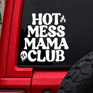 May include: A white vinyl decal applied to a vehicle window featuring the text HOT MESS MAMA CLUB in a bold, wavy font. The design includes a small flame icon next to the word HOT and a melting skull icon positioned below the word CLUB.