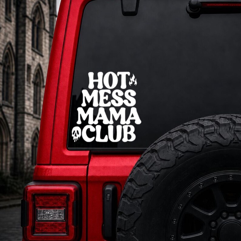 May include: A white vinyl decal applied to a vehicle window featuring the text HOT MESS MAMA CLUB in a bold, wavy font. The design includes a small flame icon next to the word HOT and a melting skull icon positioned below the word CLUB.