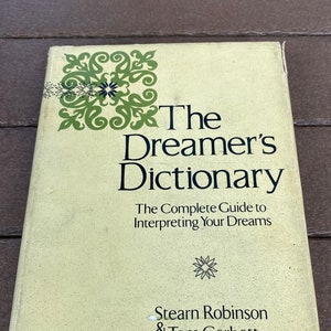 Könnte beinhalten: Ein Vintage-Buch mit dem Titel "The Dreamer's Dictionary" mit hellgelbem Einband. Der Einband zeigt grüne florale Muster und den Text "The Complete Guide to Interpreting Your Dreams." Autoren: Stearn Robinson & Tom Corbett.