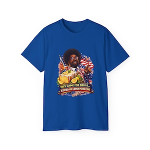 May include: Royal blue t-shirt featuring a graphic of a man with sunglasses, a suit, and an afro, holding a slice of lemon pound cake. The text on the shirt reads "THEY CAME FOR DRUGS... STAYED FOR LEMON POUND CAKE."