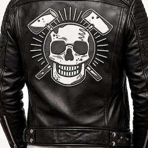 Op de afbeelding: Zwarte leren jas met een schedel en gekruiste hamers op de rug. De jas heeft een gewatteerd ontwerp op de schouders en mouwen, een ritssluiting aan de voorkant en een tailleband.