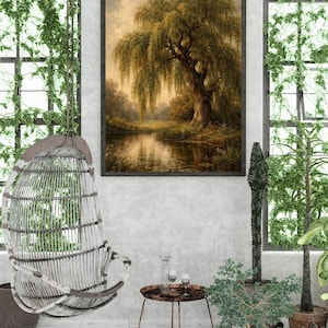 May include: A framed landscape painting depicts a weeping willow tree reflected in a calm body of water. The artwork is displayed in a bright room with a hanging chair, small table, and potted plants, creating a serene atmosphere.
